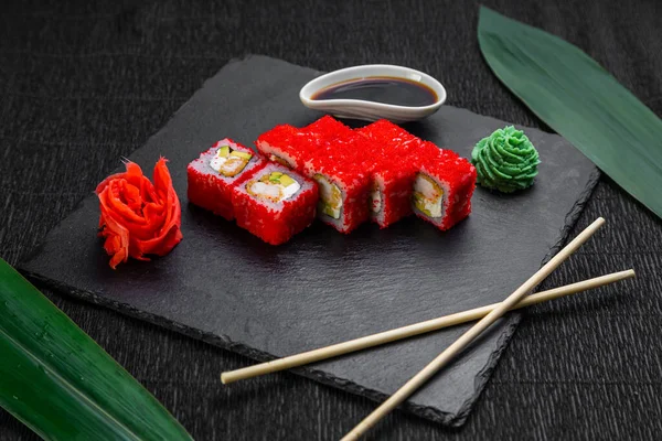 Suşi ruloları bambu yaprakları ve çubuklarla süslenmiş karanlık bir arka planda serili.
