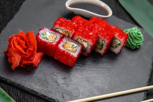 Suşi ruloları bambu yaprakları ve çubuklarla süslenmiş karanlık bir arka planda serili.