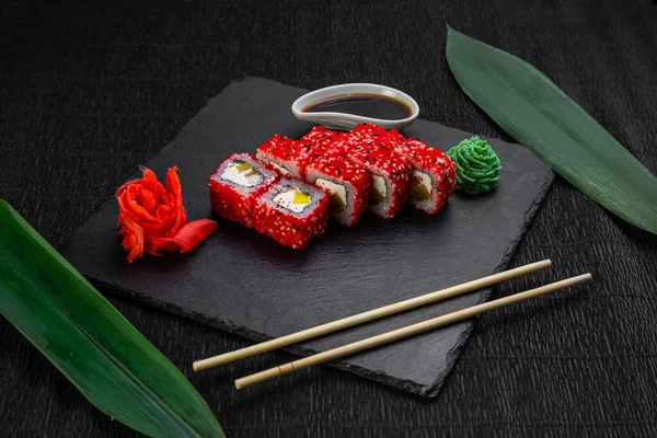 Suşi ruloları bambu yaprakları ve çubuklarla süslenmiş karanlık bir arka planda serili.