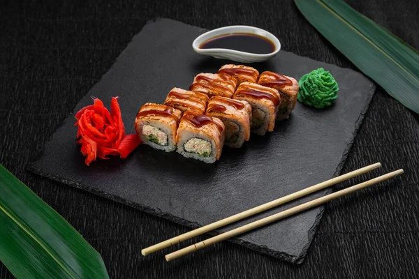 A bambuszlevelekkel és evőpálcikákkal díszített, sötét háttérre fektetett sushi tekercsek — Stock Fotó