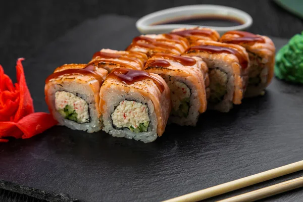 sushi rolls laid out on a dark background decorated with bamboo leaves and chopsticks