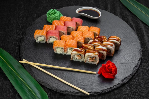 A bambuszlevelekkel és evőpálcikákkal díszített, sötét háttérre fektetett sushi tekercsek — Stock Fotó