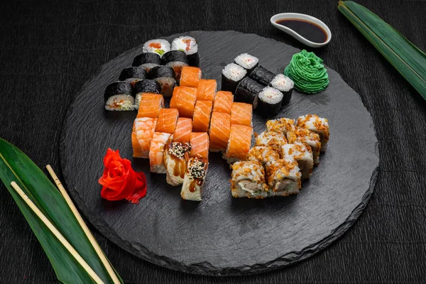 A bambuszlevelekkel és evőpálcikákkal díszített, sötét háttérre fektetett sushi tekercsek — Stock Fotó