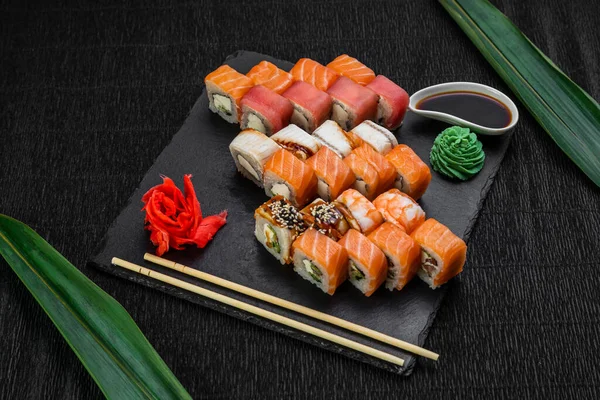 Sushi rolls laid out on a dark background decorated with bamboo leaves and chopsticks — Stock Photo, Image