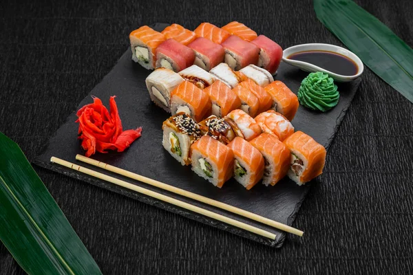 Sushi rolls laid out on a dark background decorated with bamboo leaves and chopsticks — Stock Photo, Image