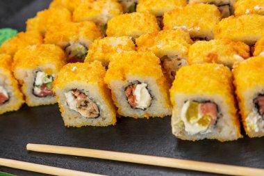 Suşi ruloları bambu yaprakları ve çubuklarla süslenmiş karanlık bir arka planda serili.