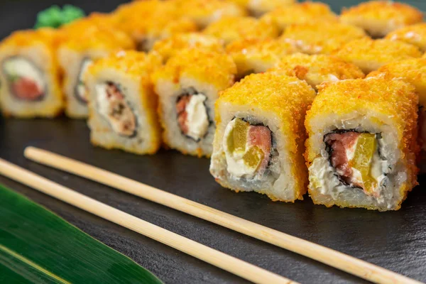 Suşi ruloları bambu yaprakları ve çubuklarla süslenmiş karanlık bir arka planda serili.