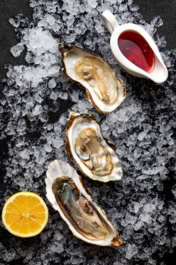 Açılmış taze istiridyeler, buzun üstünde, karanlık bir arka planda.