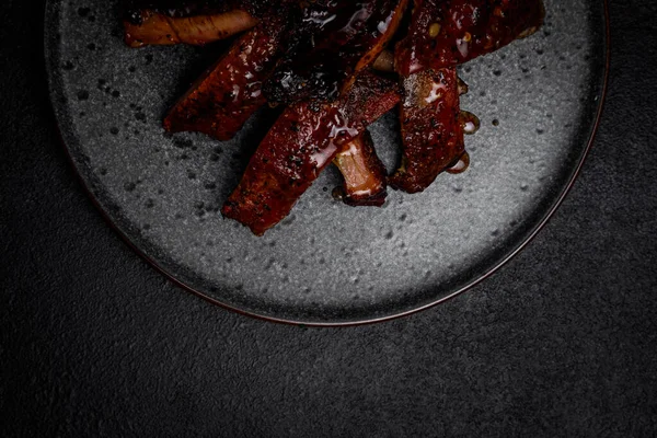 Geräucherte Rippen in Sauce auf einem Teller vor dunklem Hintergrund — Stockfoto
