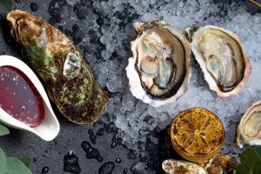 Deniz lezzeti açık istiridyeler koyu bir arka planda buzun üzerine serilmiş. Arka plan okaliptüs dalları, limon, kapalı istiridye ve sos ile süslenmiştir..