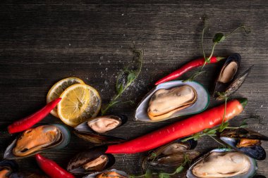 Ahşap bir zeminde pişirilmiş midye, arka plan yeşillik, biber, mikroyeşillik, tuz ile süslenmiş.