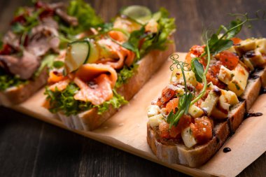 Et, balık ve çeşitli mikro yeşilliklerle doldurulmuş üç farklı tapas tabağı koyu bir arka planda servis edilir.