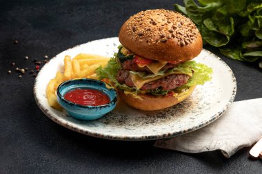 Kızarmış biftek, sebze ve peynirli hamburger patates kızartması ve sosla servis edilir.