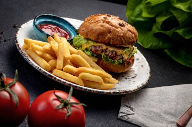 Kızarmış biftek, sebze ve peynirli hamburger patates kızartması ve sosla servis edilir.