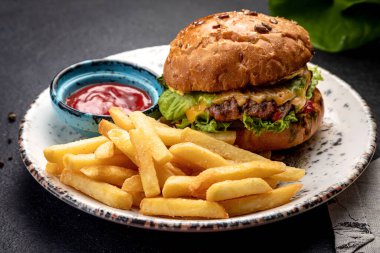 Kızarmış biftek, sebze ve peynirli hamburger patates kızartması ve sosla servis edilir.