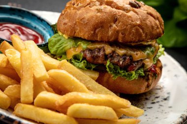 Kızarmış biftek, sebze ve peynirli hamburger patates kızartması ve sosla servis edilir.