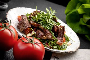 Biftek salatası, roka ve vişneli domates, koyu arkaplanda.