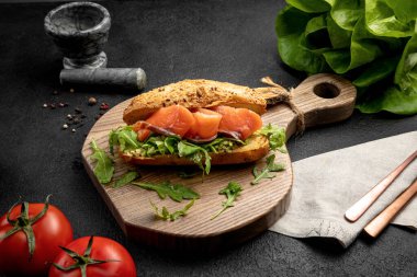 Somon balıklı sandviç ve roka. Koyu bir arka planda tahta bir tahtada servis ediliyor.