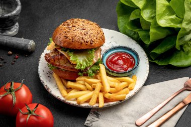 Biftek, marul ve peynirli hamburger. Koyu bir arka planda patates kızartması ve sos ile servis edilir.