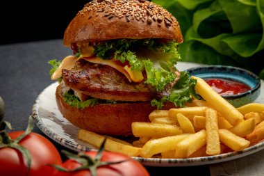 Biftek, marul ve peynirli hamburger. Koyu bir arka planda patates kızartması ve sos ile servis edilir.