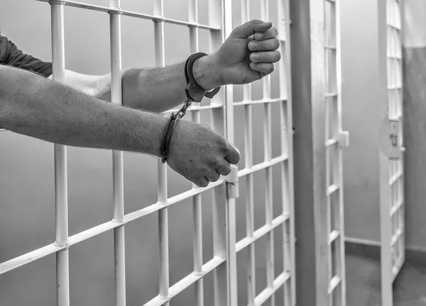 Prisoner in handcuffs locked in a cell. B&W. — Stock Photo, Image