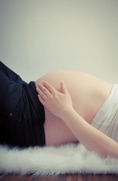 Hand houden zwangere buik liggend op witte vacht — Stockfoto