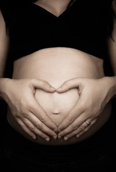 Gravid kvinna att göra hjärtat form med händerna över magen — Stockfoto