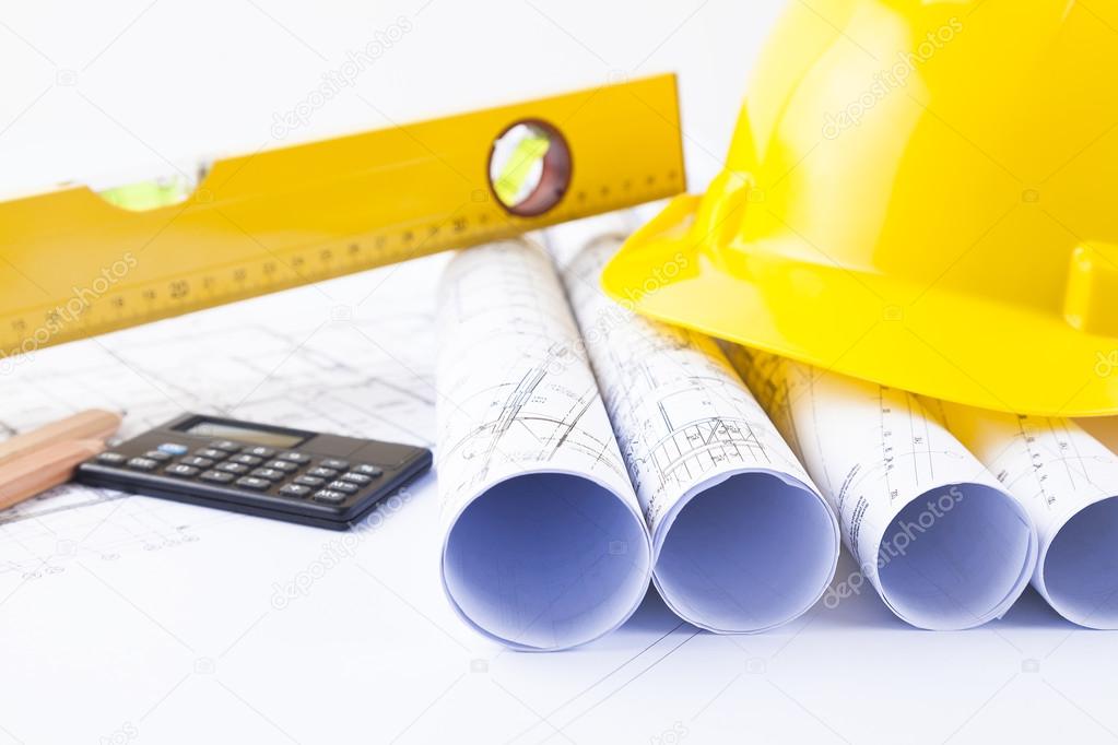 Yellow helmet and heap of project drawings and construction tools