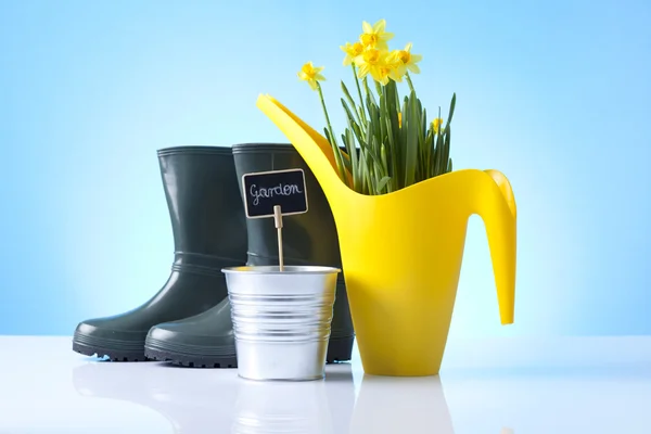 Gießkanne und Gartenstiefel auf blauem Hintergrund — Stockfoto