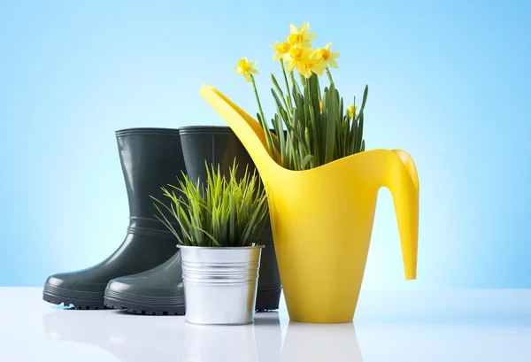 Gießkanne und Gartenstiefel auf blauem Hintergrund — Stockfoto