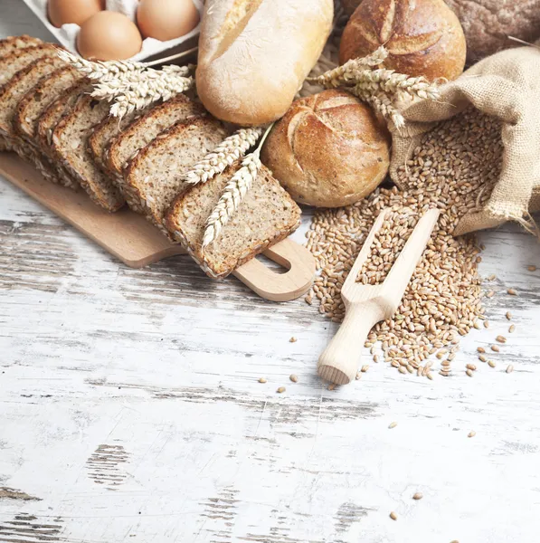 Pane rustico e grano su un vecchio tavolo di legno fasciato d'epoca. sfondo con spazio di testo libero — Foto Stock