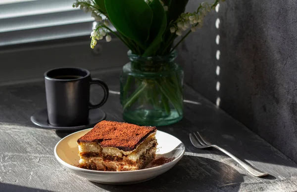 Традиційний італійський десерт тірамісу, кава і букет лілій долини на сірому бетонному тлі.. — стокове фото