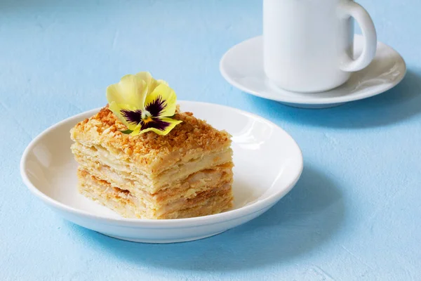 Шматочок торта Наполеона, прикрашений квіткою віолончелі, подається з чашкою кави або чаю . — стокове фото