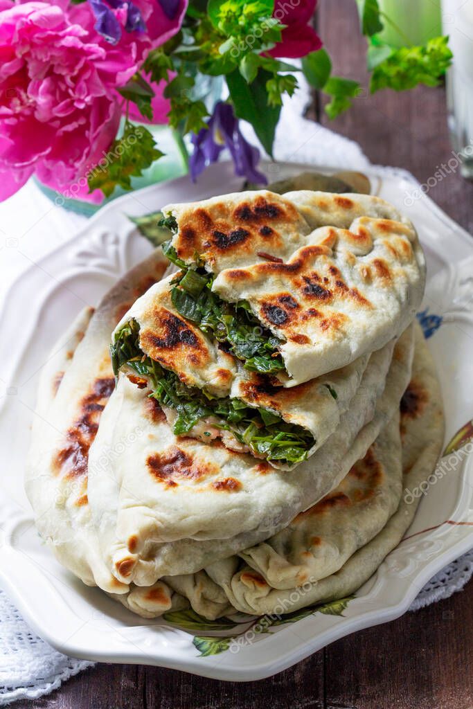 Traditional Armenian flatbread with greens zhengyalov hats, served with yogurt on the background of a bouquet. Selective focus.