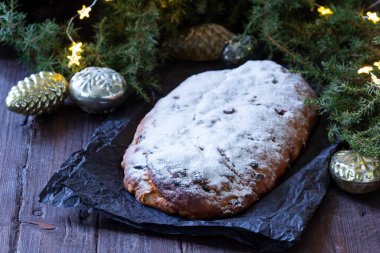 Christmas stollen with dried fruits, nuts and spices, Christmas decorations on a dark wooden background. Rustic style, selective focus.