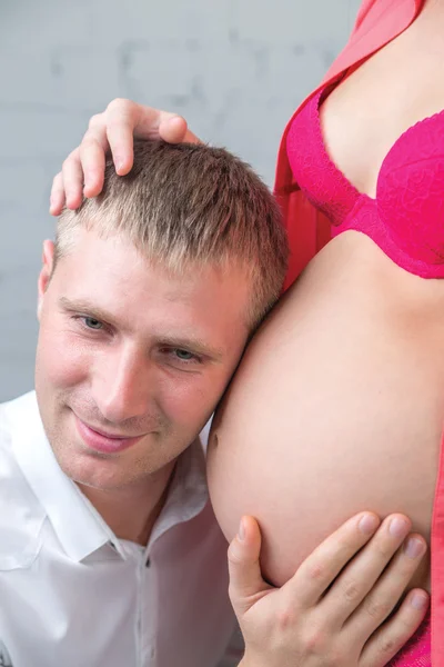 Young man put head on wife pregnant belly in red — Stock Photo, Image