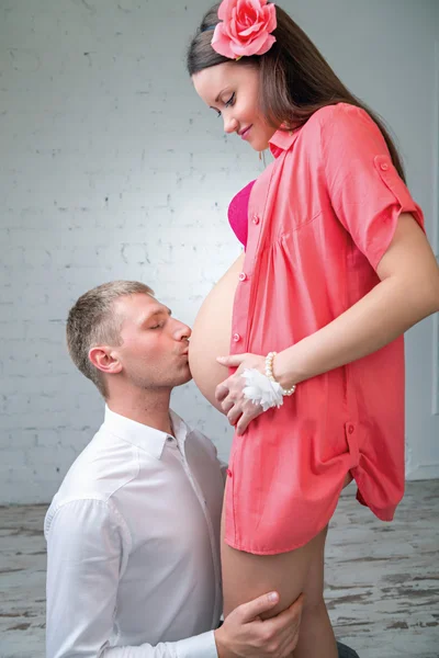 Young man kisses the belly of pregnant wife in red — Stock Photo, Image