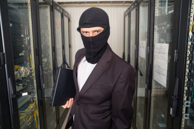 robber in black mask hack server room downloading data on laptop clipart