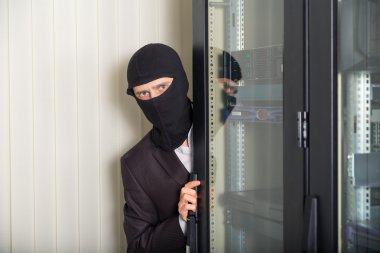 Robber in black mask hack server room downloading data on laptop clipart
