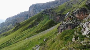 Büyük yamaçta kayalar, tepesinde çimenler ve şelale var.