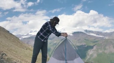 Şapkalı bayan turist yamaçtaki kayalık zeminde çadır kuruyor.