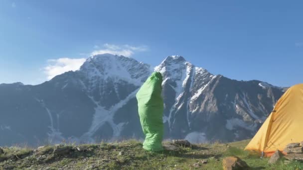 Homem no saco de dormir salta para cima no topo da encosta perto da tenda — Vídeo de Stock