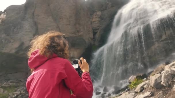 Señora hace vídeo en la cámara de pie cerca de la cascada alta — Vídeos de Stock