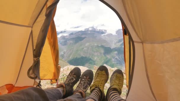 Persons lie in tent and wave legs in boots against mountains — Stock Video