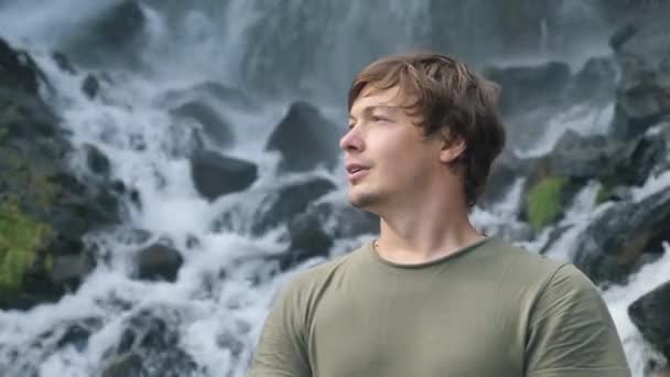 Man inhaleert lucht en poseert kijkend in camera bij waterval — Stockvideo
