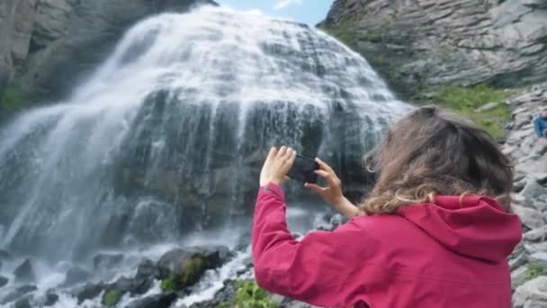 Lady segura telefone e faz vídeo em pé perto de cachoeira — Vídeo de Stock