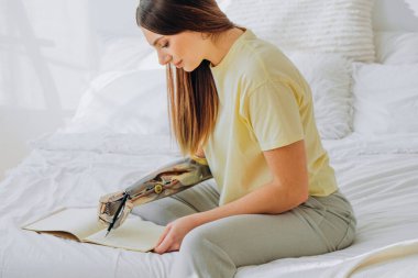 Kadın dizüstü bilgisayarda biyonik koluyla yatakta oturuyor.