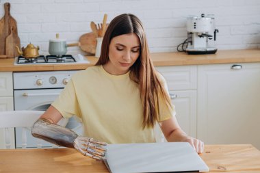 Biyonik kolu olan genç bir kadın internette dizüstü bilgisayarda sörf yapıyor.