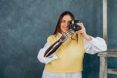 Metal biyonik kollu genç bir kadın gri renkte fotoğraf çekiyor.