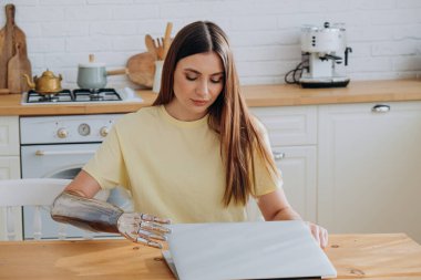 Biyonik kolu olan genç bir kadın internette dizüstü bilgisayarda sörf yapıyor.